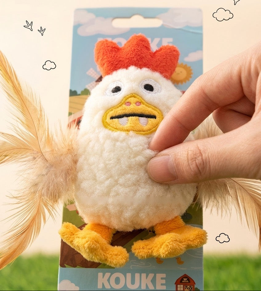 A hand holds a plush chicken-shaped pet toy attached to a printed backing card. The toy has a white fuzzy body, orange comb, yellow beak and feet, and attached feather wings.