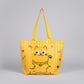 Yellow tote bag with cartoon cat design held by a hand on a white surface