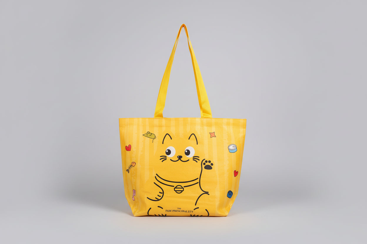 Yellow tote bag with cartoon cat design held by a hand on a white surface