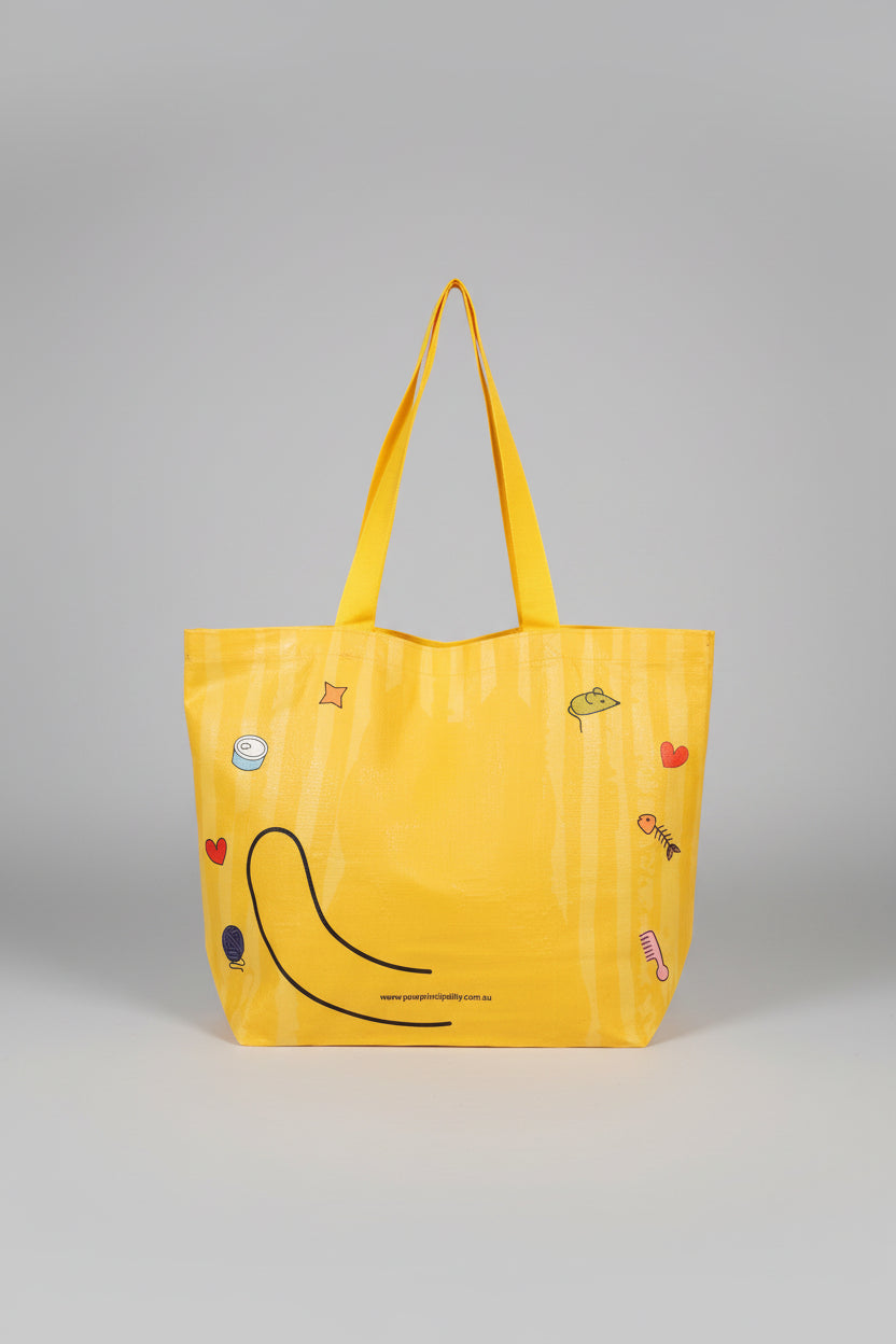Yellow tote bag cat with cartoon designs held by a hand on a white surface